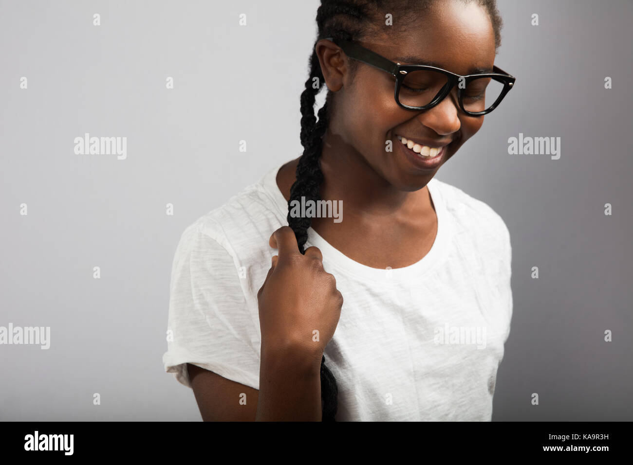 Mujer con cabello trenzado el uso de anteojos sobre fondo gris Foto de stock