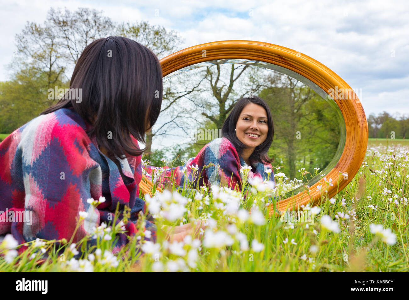 Joven mujer colombiana acostado con espejo en el florido prado Foto de stock