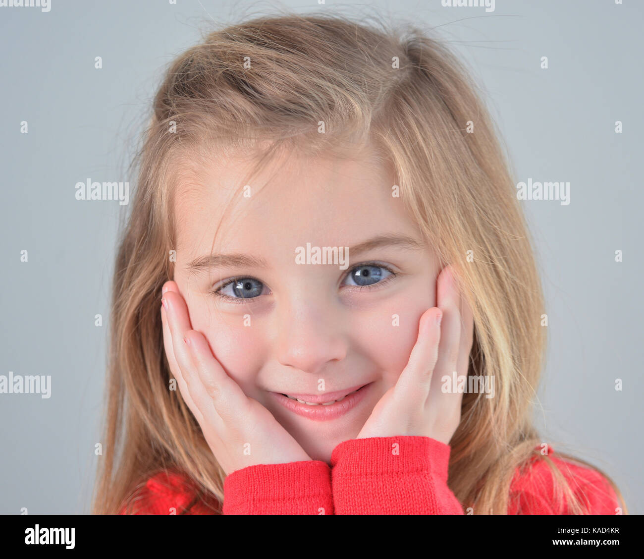 Pequeña sonriente chica rubia con ojos azules, remera roja Foto de stock