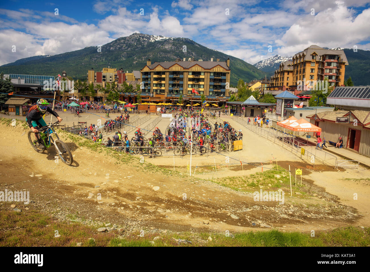 Biker montando una bicicleta de montaña en el Whistler Mountain bike park con muchos ciclistas esperando en la línea de fondo. Foto de stock