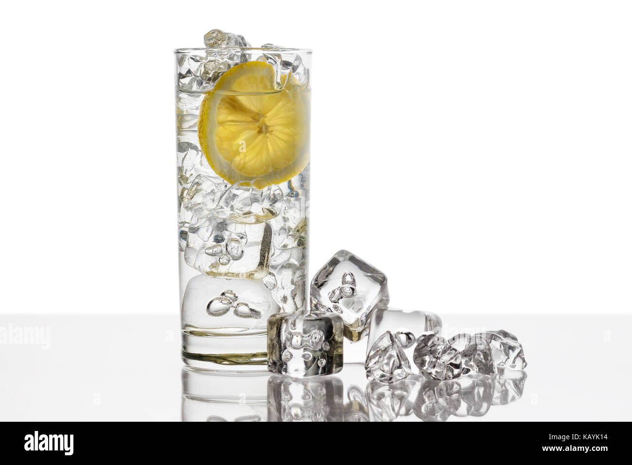 Vaso lleno de agua fresca con la rodaja de limón y cubitos de hielo al fondo Foto de stock