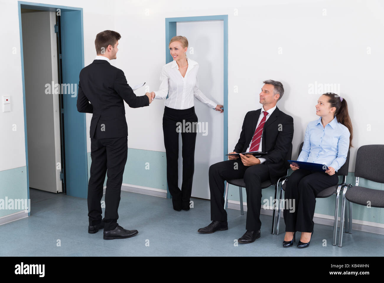 La empresaria un apretón de manos con el hombre delante de gente esperando para una entrevista de trabajo en Office Foto de stock