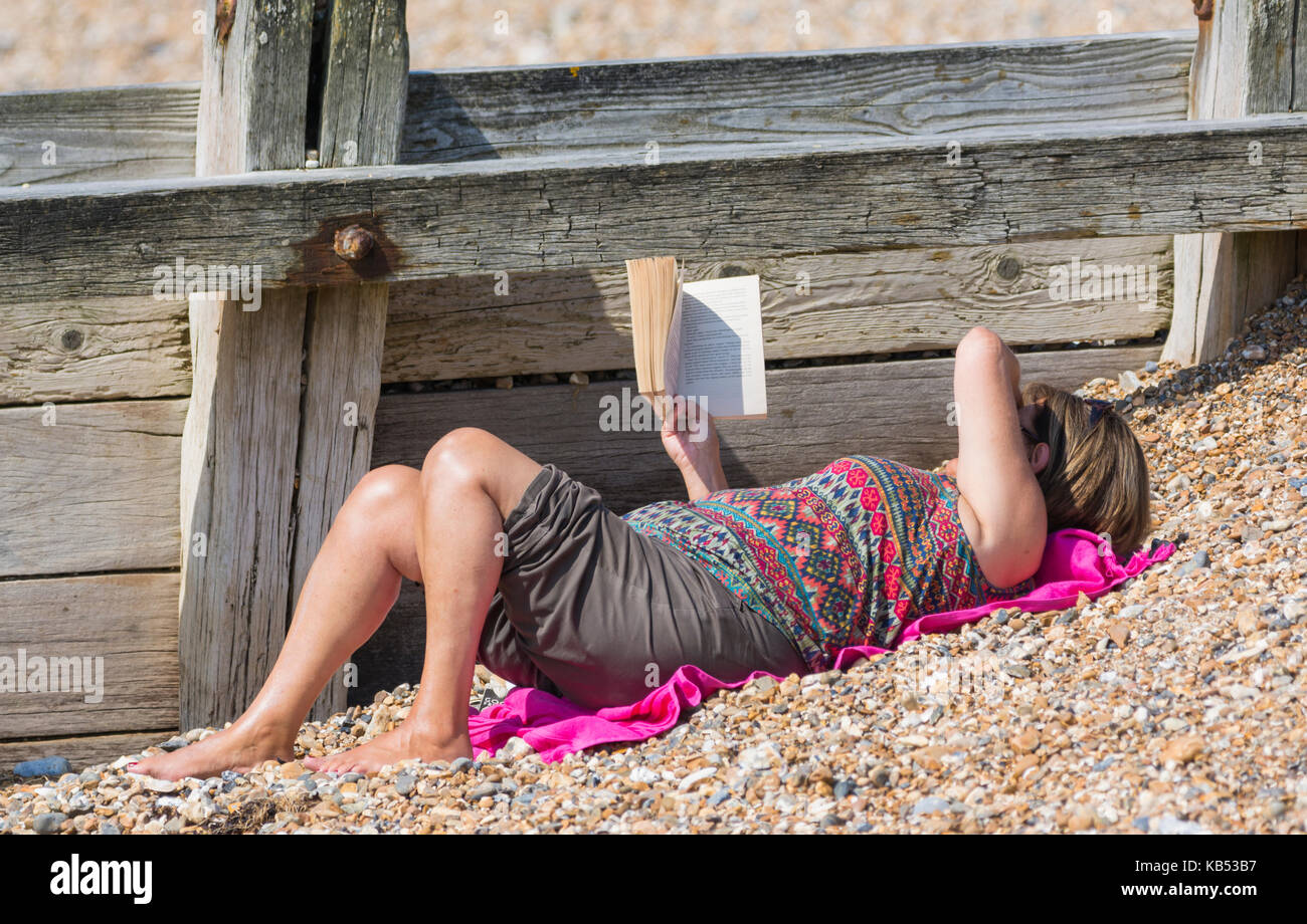 Mujer recostada sobre una playa leyendo un libro. Foto de stock