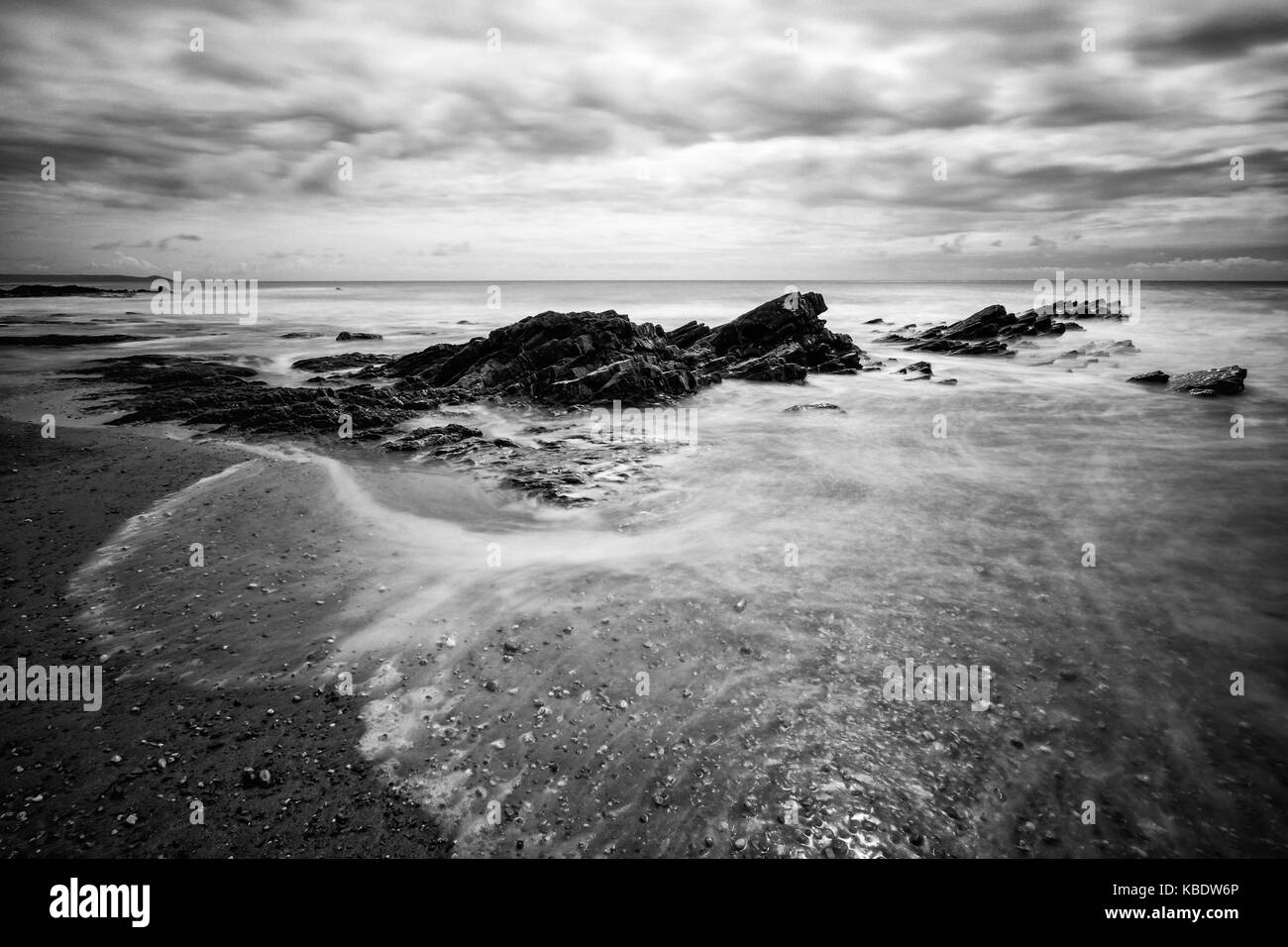 Piedras irregulares y agua blanda bañando en la playa. Esta imagen fue tomada en seaton, Cornualles, en el Reino Unido. Foto de stock