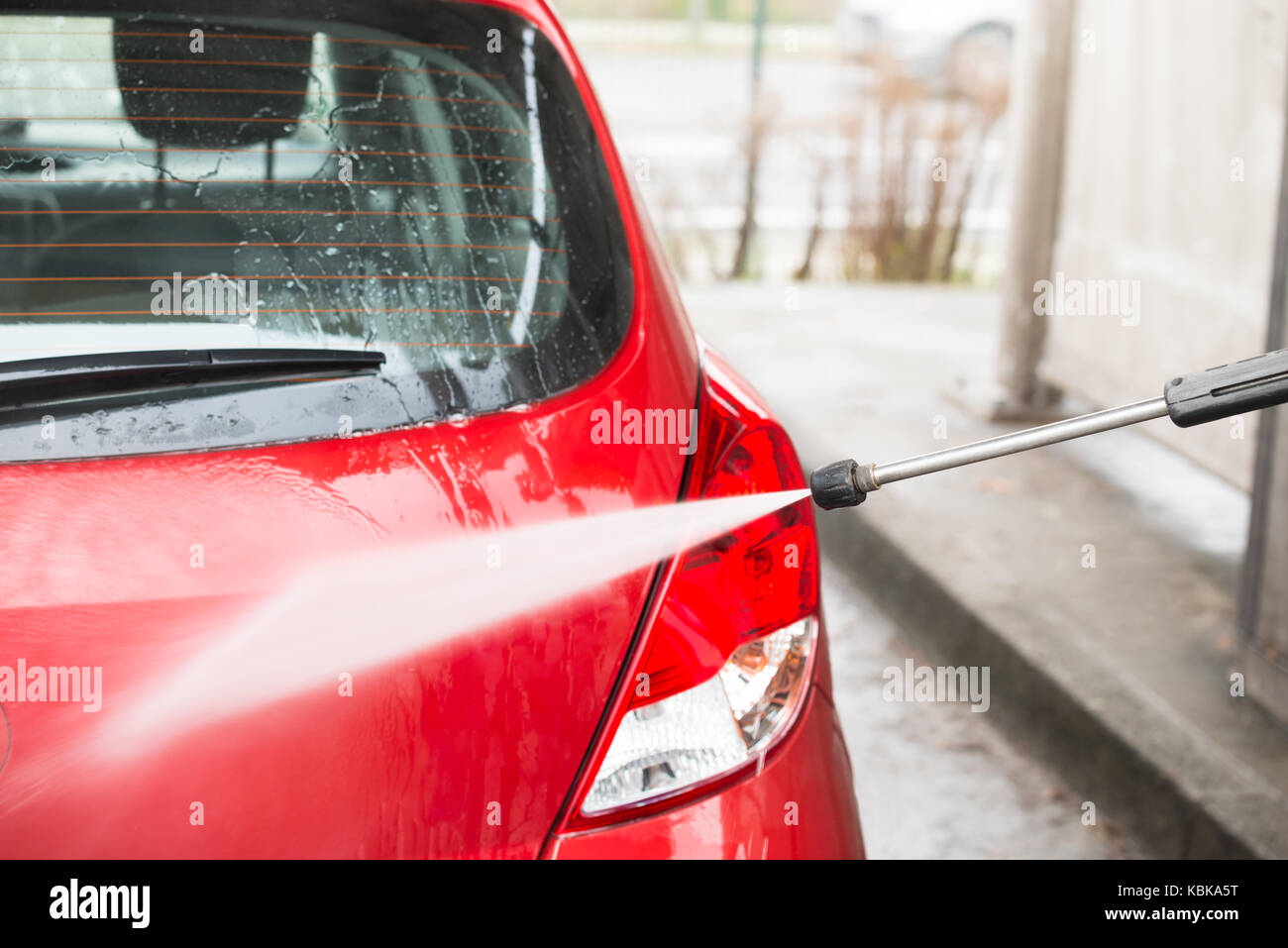 Coche rojo de lavado con chorro de agua de alta presión en la estación de servicio Foto de stock