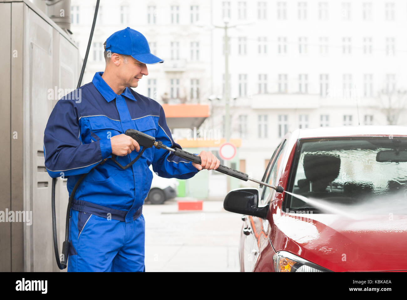 Mature voluntario con el chorro de agua de alta presión de lavado de coche rojo en la estación de servicio Foto de stock