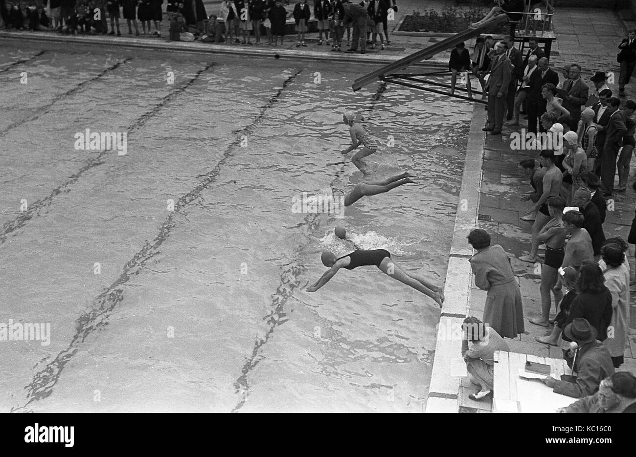 1950s, históricos, las niñas participan en una gala de natación, con algo de buceo en para iniciar la carrera, otros saltan, apoyada por los padres y otros competidores, Inglaterra, Reino Unido. Foto de stock