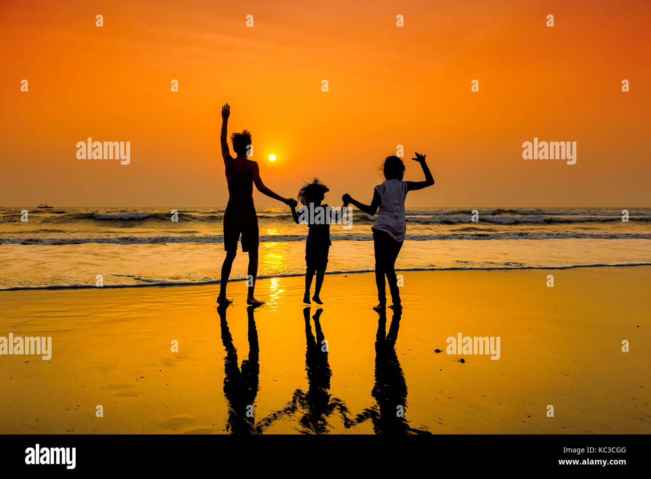 Las siluetas del grupo de niños bailando en la playa al atardecer. Foto de stock