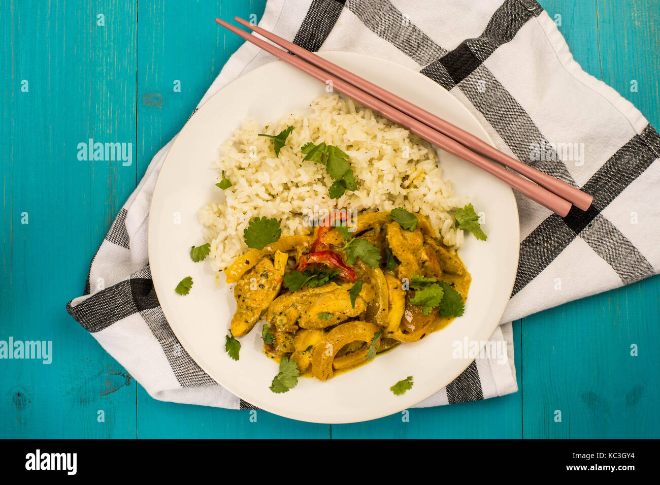 Estilo tailandés curry panang de pollo con arroz jazmín contra un fondo de madera azul sobre un paño de color rosa con chop sticks Foto de stock