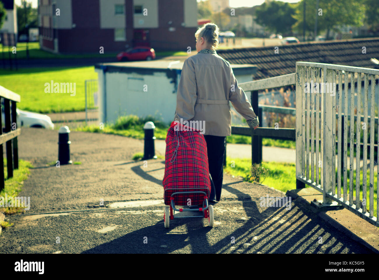 Anciana con tartan shopping bag trolley cruzando el puente del canal Forth and Clyde knightswood desde atrás vista trasera iluminada desde atrás Foto de stock