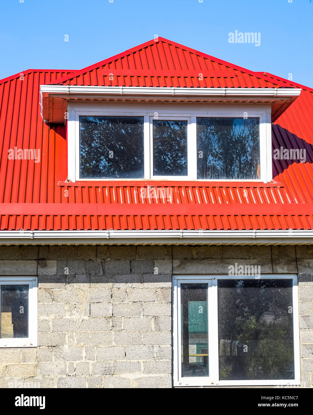 himno Nacional director ladrar Casa con ventanas de plástico rojo y un techo de chapa corrugada. Techos de  perfil metálico forma ondulada en la casa con ventanas de plástico. Casa de  ceniza Fotografía de stock -