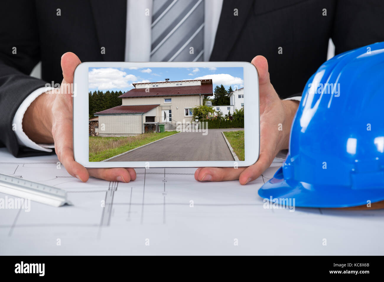 Close-up de macho joven arquitecto que muestra una casa en tableta digital más blueprint en Office Foto de stock