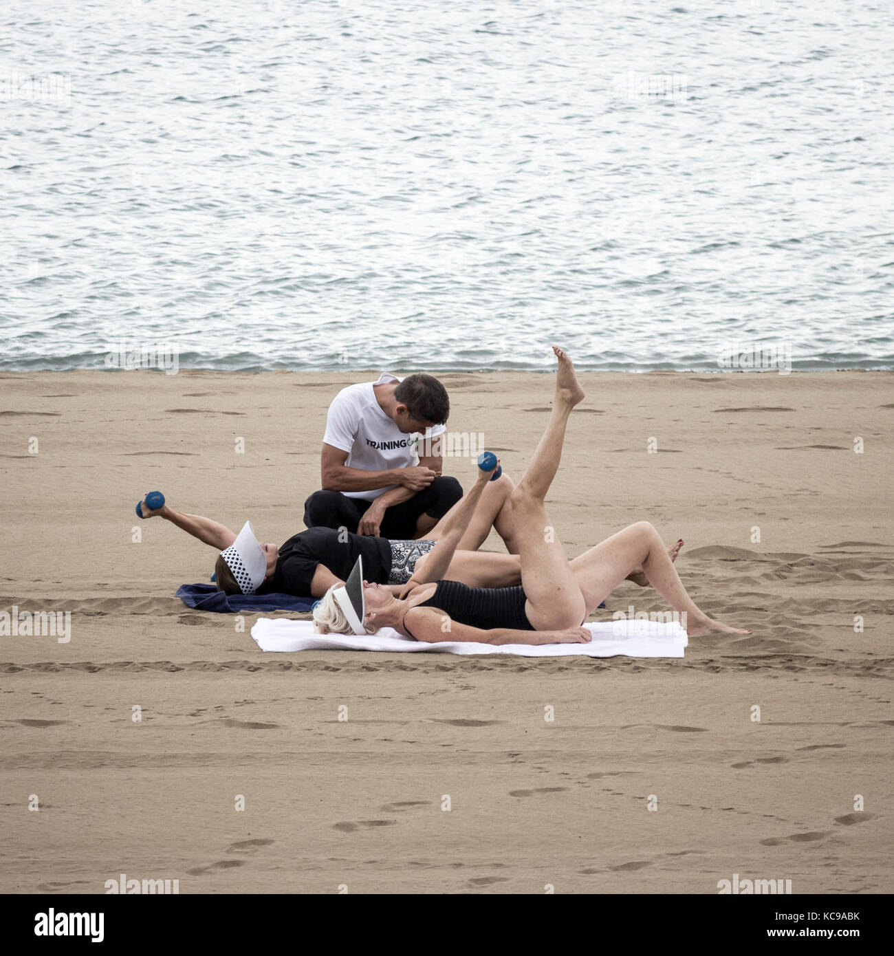 Entrenador personal en la playa supervisando con dos mujeres mayores levantando pesas. Foto de stock