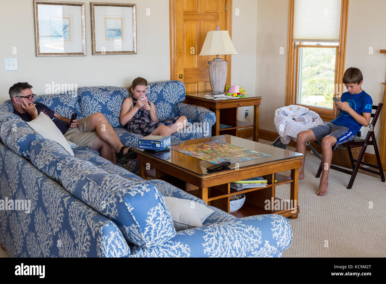Avon, Outer Banks, Carolina del Norte, EE.UU. American Family utilizando teléfonos celulares y dispositivos de juegos móviles en el Salón, mientras que en la Casa de vacaciones en la playa. Foto de stock