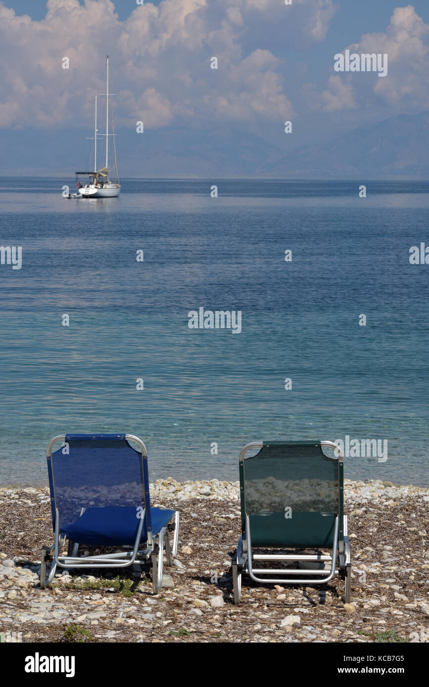 Dos tumbonas vacías o hamacas en la playa con un yate de lujo anclado en la  bahía. azul mediterráneo de aguas en entorno paradisíaco en la playa  Fotografía de stock - Alamy