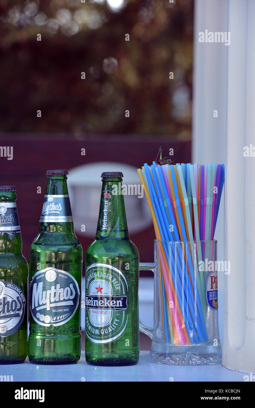 La cerveza embotellada y cervezas en un bar junto a un vaso o recipiente  lleno de plástico multicolor pajas. Las botellas de cerveza de cristal  verde lleno de ale Fotografía de stock -