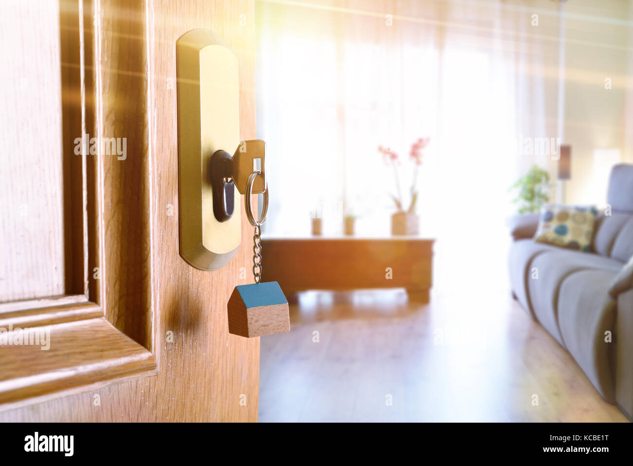 Abrir puerta de entrada detalle de una casa con las llaves en la cerradura y sala amueblada en el fondo con el efecto de luz dorada. Foto de stock