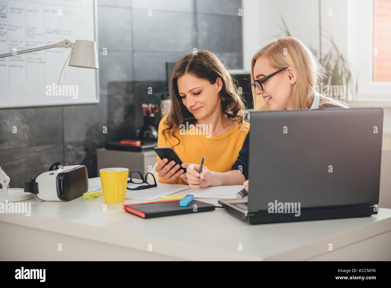 Dos mujer de negocios trabajando juntos en la oficina, con teléfonos inteligentes y escribir notas Foto de stock