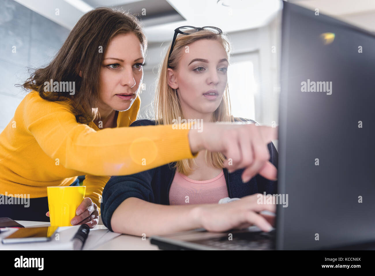 Dos mujeres que trabajan en la oficina y el uso de ordenador portátil mientras uno esté apuntando a la laptop Foto de stock