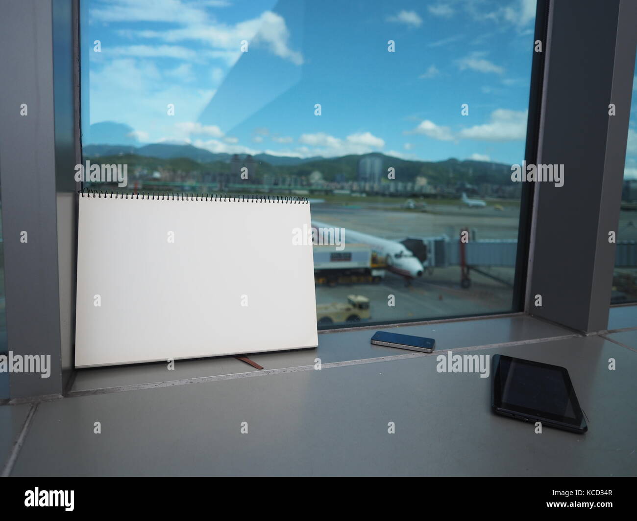 Nota libro blanco con el teléfono inteligente en la ventana en el aeropuerto Foto de stock