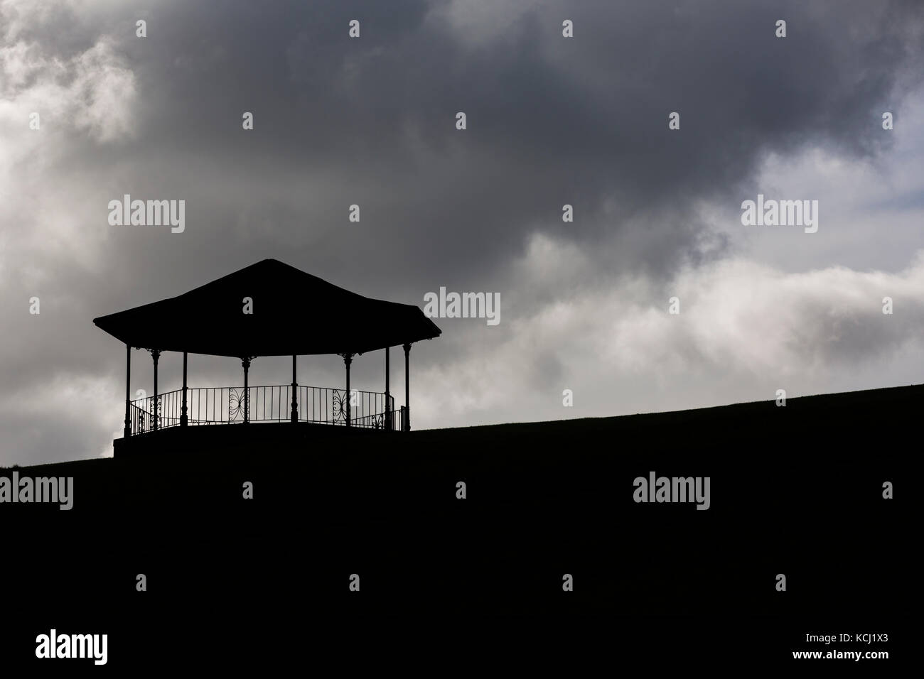 Silueta de quiosco en la cima de la colina contra la oscuridad, Moody nubes en el cielo Foto de stock