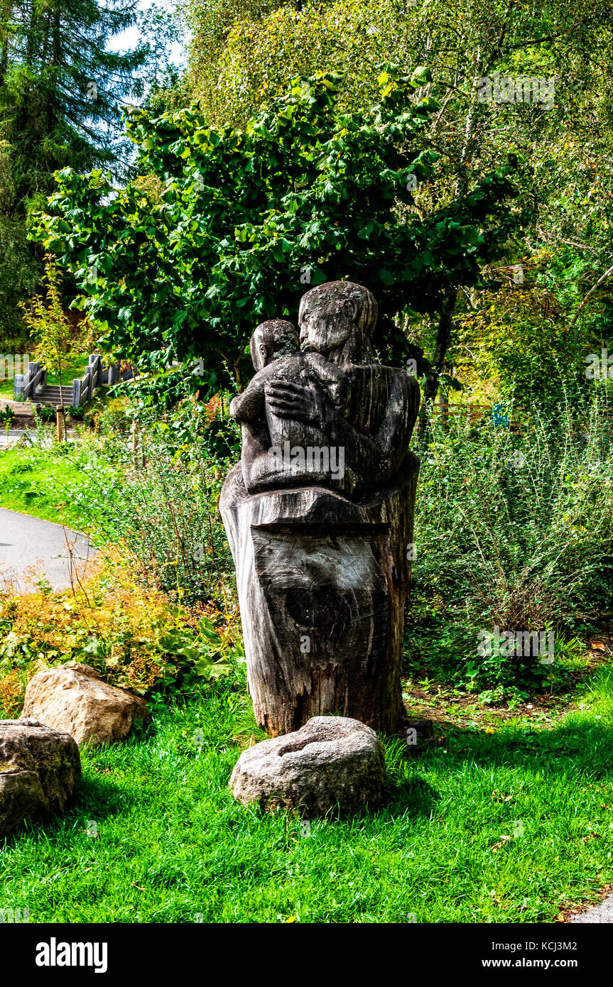 Un tronco de madera tallada en una escultura de una persona sosteniendo un bebé, mitad en sombra en el área boscosa de Queen's Ver centro de recepción de visitantes Foto de stock