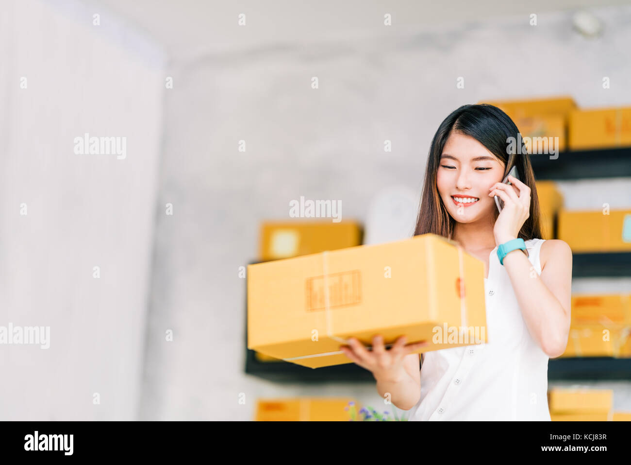 Los propietarios de pequeñas empresas, la mujer asiática mantenga paquete de verificación, con llamada de teléfono móvil Recepción de orden de compra, el trabajo en la oficina principal de entrega de marketing online. Foto de stock