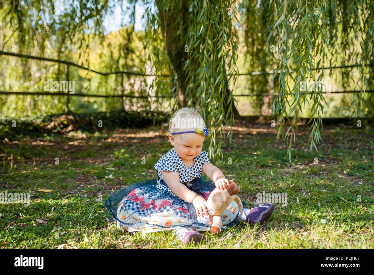 Niña sentada en el pasto y jugar con su osito de peluche Foto de stock