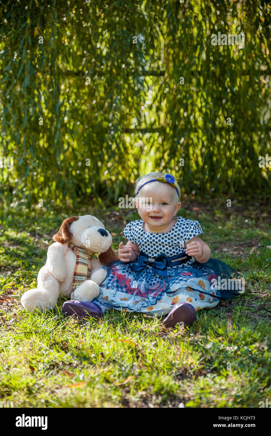 Niña sentada en el pasto y jugar con su osito de peluche Foto de stock