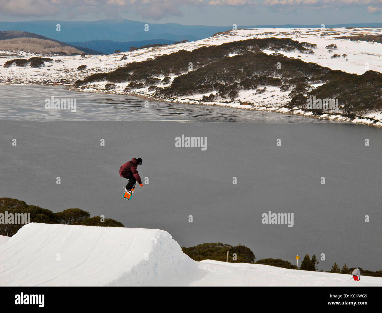 Snowboarder a mitad de salto por encima de la represa Rocky Valley, parte del esquema hidroeléctrico Kiewa. Falls Creek, Parque Nacional Alpine, Victoria, Australia Foto de stock