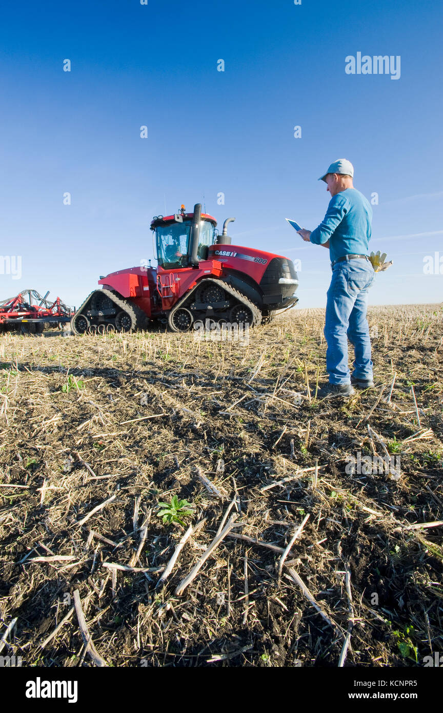 Agricultor usando un Tablet en la parte delantera del tractor y la sembradora neumática, la siembra de trigo de invierno en un campo de labranza cero con rastrojo de canola, cerca de Lorette, Manitoba, Canadá Foto de stock