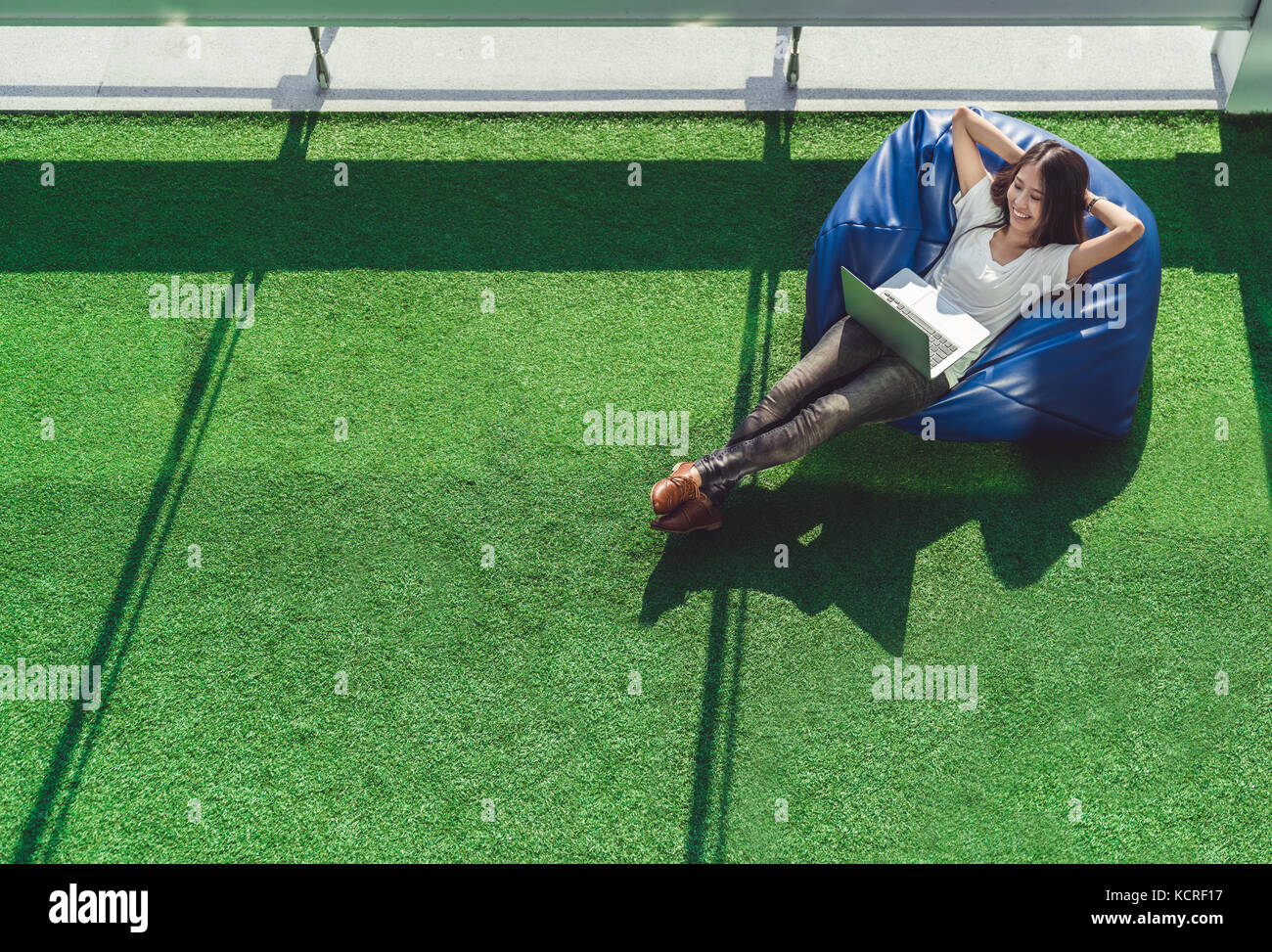 Estudiante universitario de Asia o freelance mujer utilizando equipo portátil, tumbado sobre bean bag en jardín. campus universitario o parque escena. Foto de stock