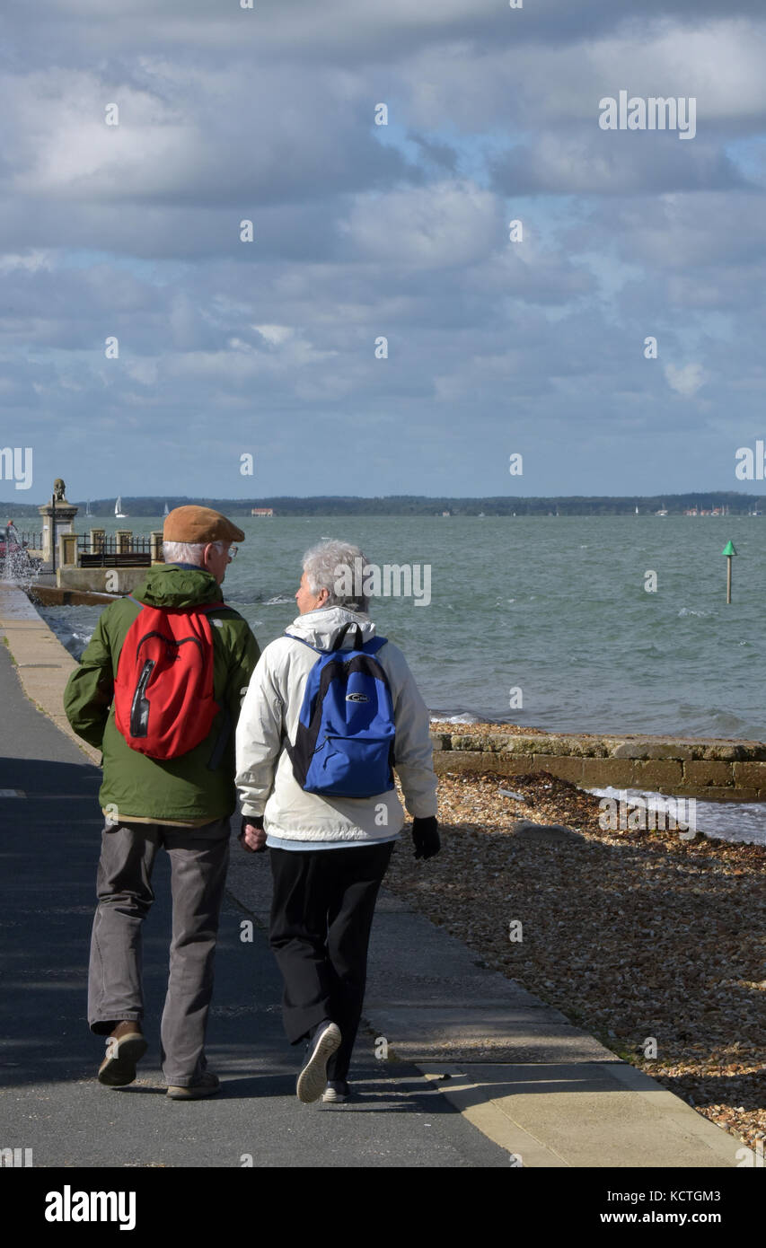 Dos personas de edad o una pareja de ancianos caminando por el paseo  marítimo en Cowes en la isla de Wight llevar mochilas azules y rojas  Fotografía de stock - Alamy