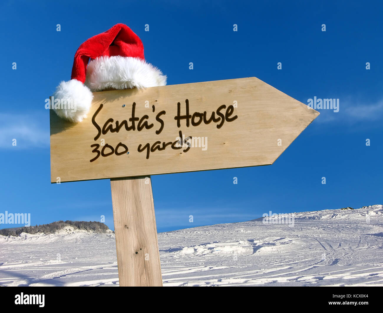 Cartel de madera con gorro de Santa Claus indicando la casa de Papá Noel,  con la nieve y el cielo de fondo azul Fotografía de stock - Alamy