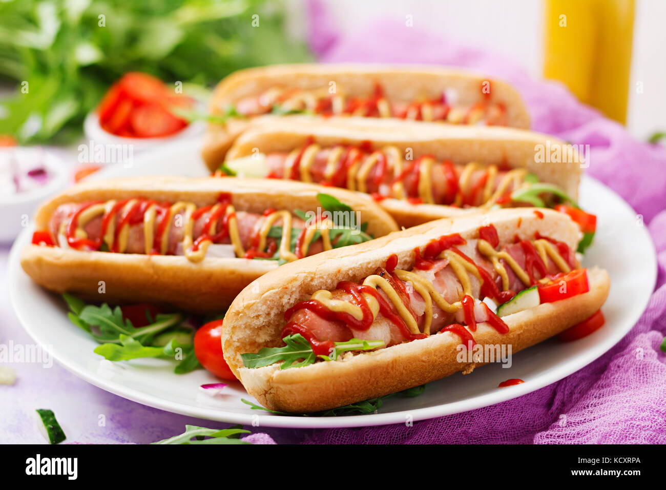 Hot Dog con salchicha, tocino, pepino, tomate y cebolla roja en la placa blanca Fotografía de Hot Dog con salchicha, tocino, pepino, tomate y cebolla roja en la placa blanca Fotografía de