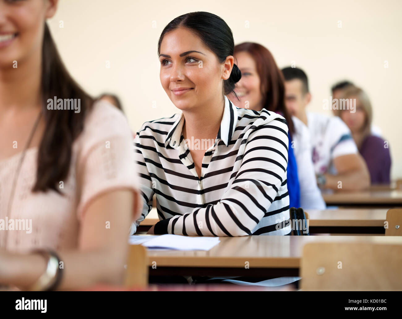 Alegre estudiante universitario femenino sentado en un aula llena de estudiantes Foto de stock