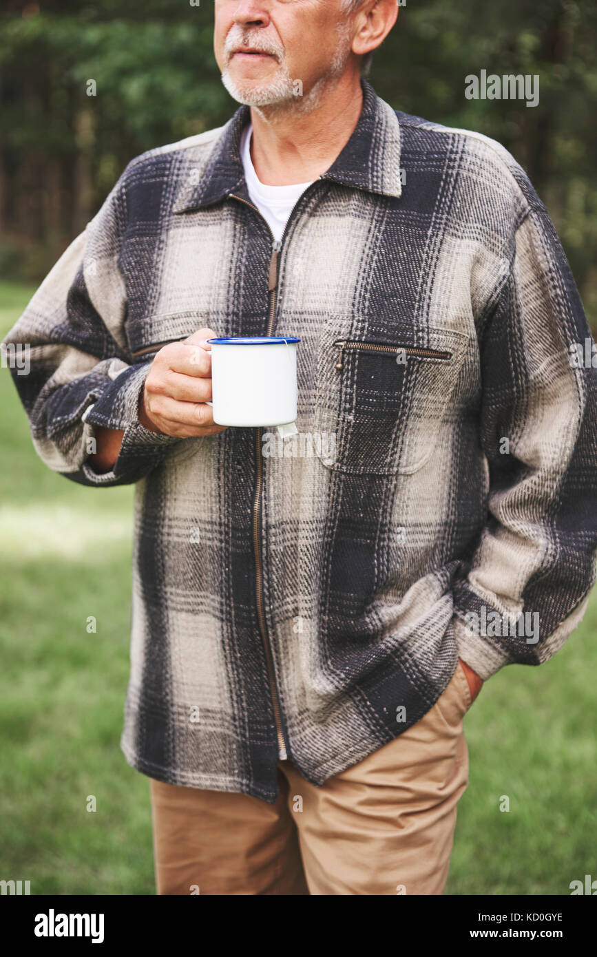 Hombre de pie senior en entorno rural, sosteniendo tin cup Foto de stock