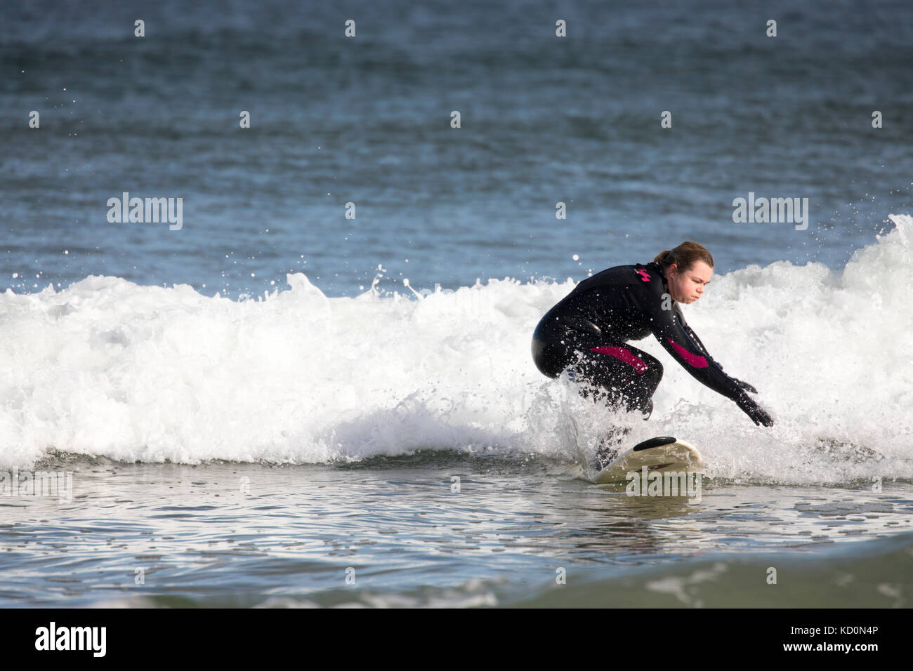 Surfista hembra montando una ola en las frías aguas de Lossiemouth, Escocia usando un traje de neopreno de cuerpo entero y concentrándose en mantenerse erguido en la tabla de surf, Escocia, Reino Unido Foto de stock