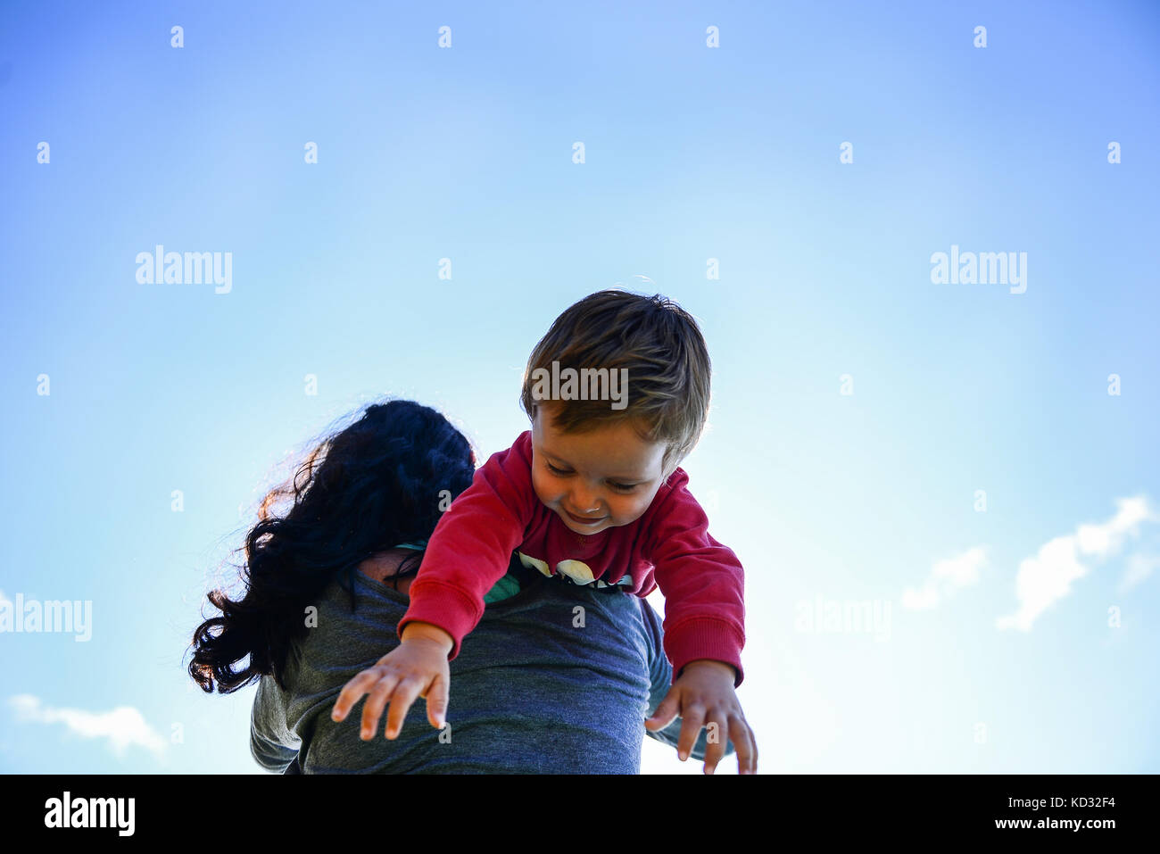 Ángulo de visión baja de niño masculino sobre el hombro de la madre contra el cielo azul Foto de stock