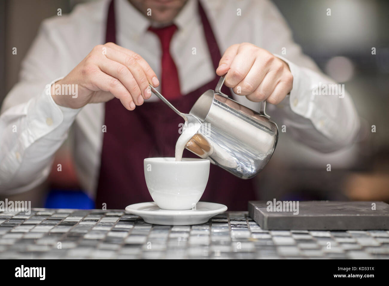 Mesero en un restaurante, vierte la leche en la taza de café, sección  intermedia Fotografía de stock - Alamy