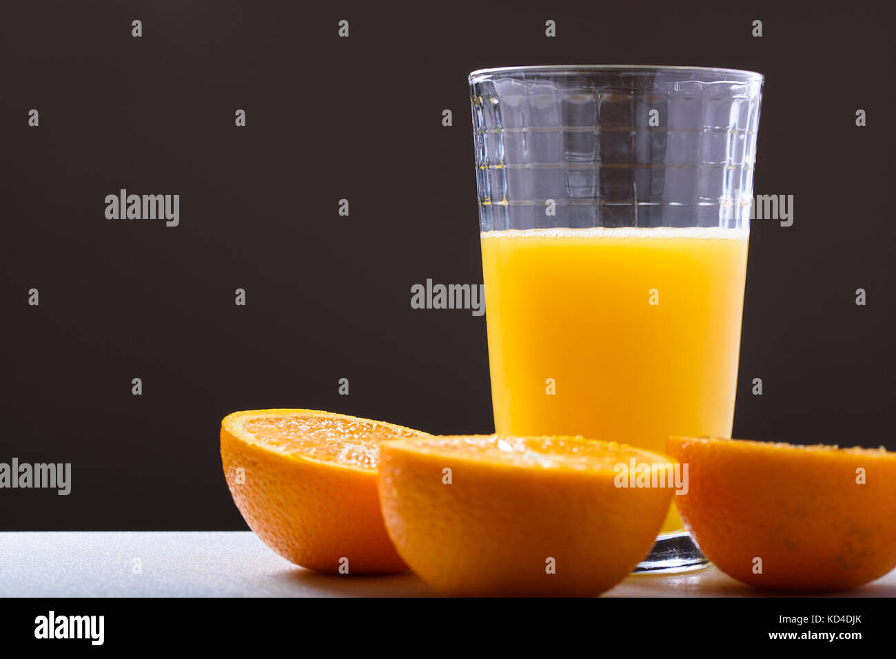 Vaso de jugo de naranja fresco junto con las mitades de naranja sobre un fondo oscuro, vista lateral Foto de stock