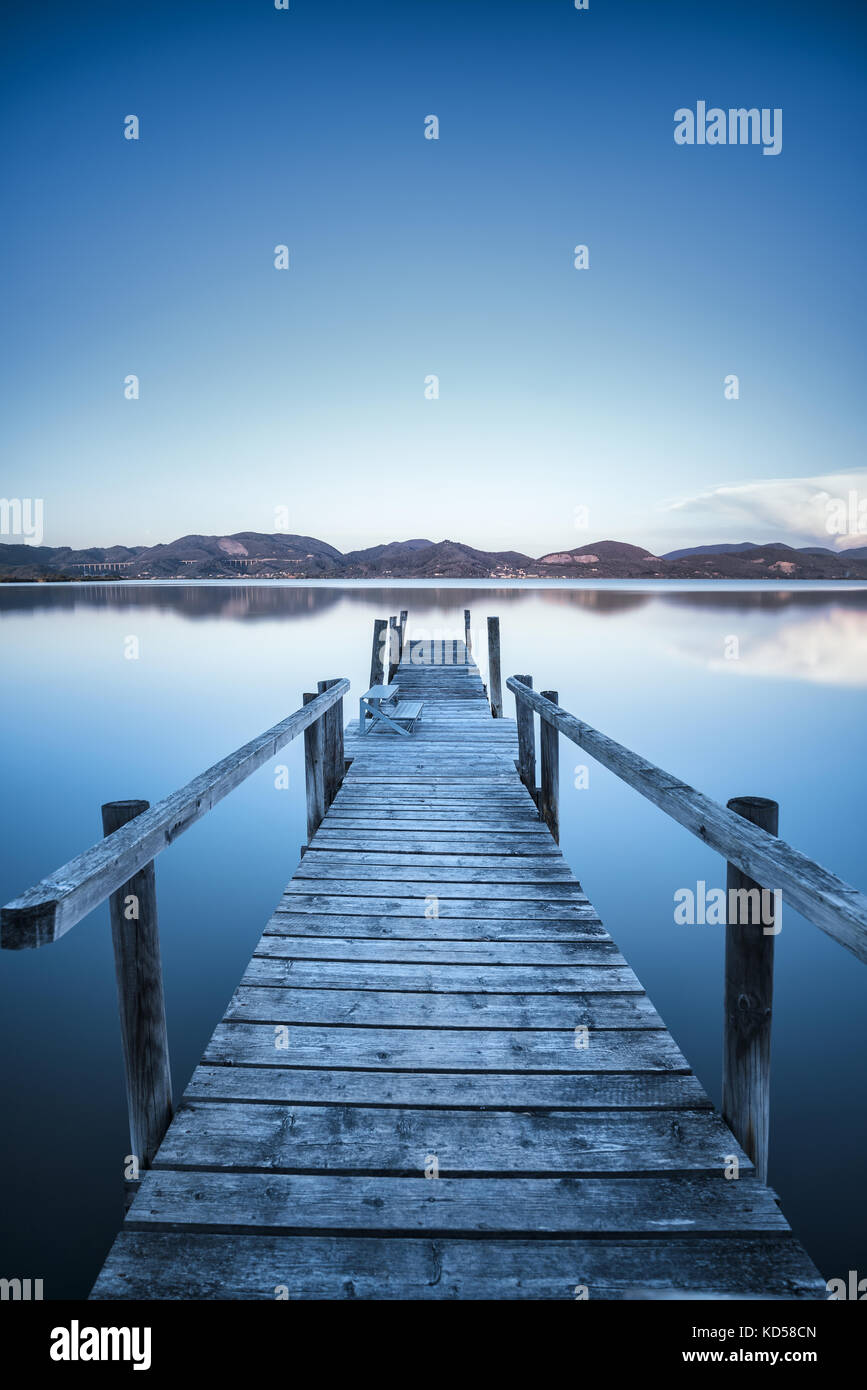 Muelle de madera o el embarcadero del lago azul cielo del atardecer y la reflexión del agua. Una exposición larga, Versilia massaciuccoli, Toscana, Italia. Foto de stock