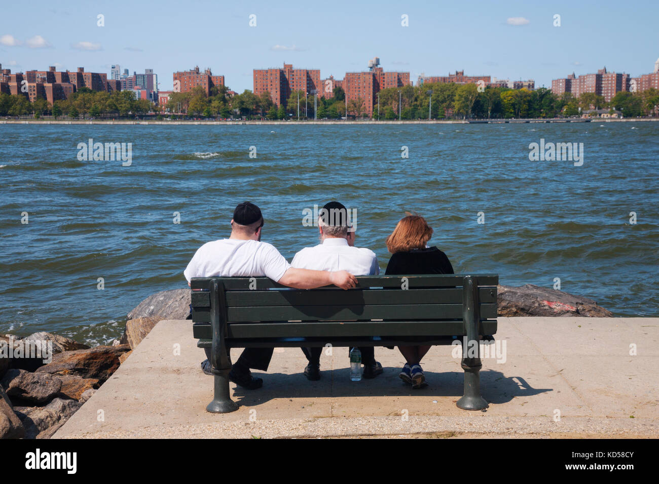 Dos hombre judío y una mujer sentada en un banco público en día soleado cerca del East River de Nueva York Foto de stock
