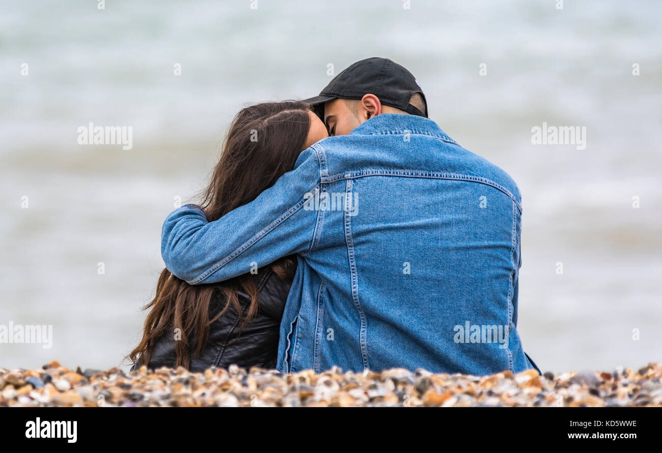 Pareja joven sentado en una playa a besar y abrazar el uno al otro. Los jóvenes amantes abrazos en la playa. Foto de stock