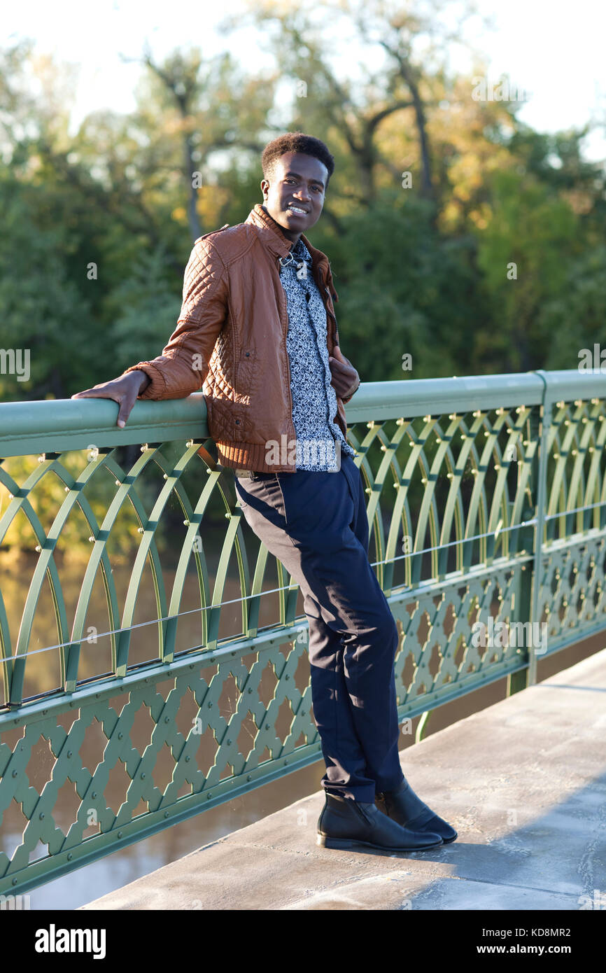 Apuesto joven negro se inclina sobre la barandilla de un puente sobre un río Foto de stock