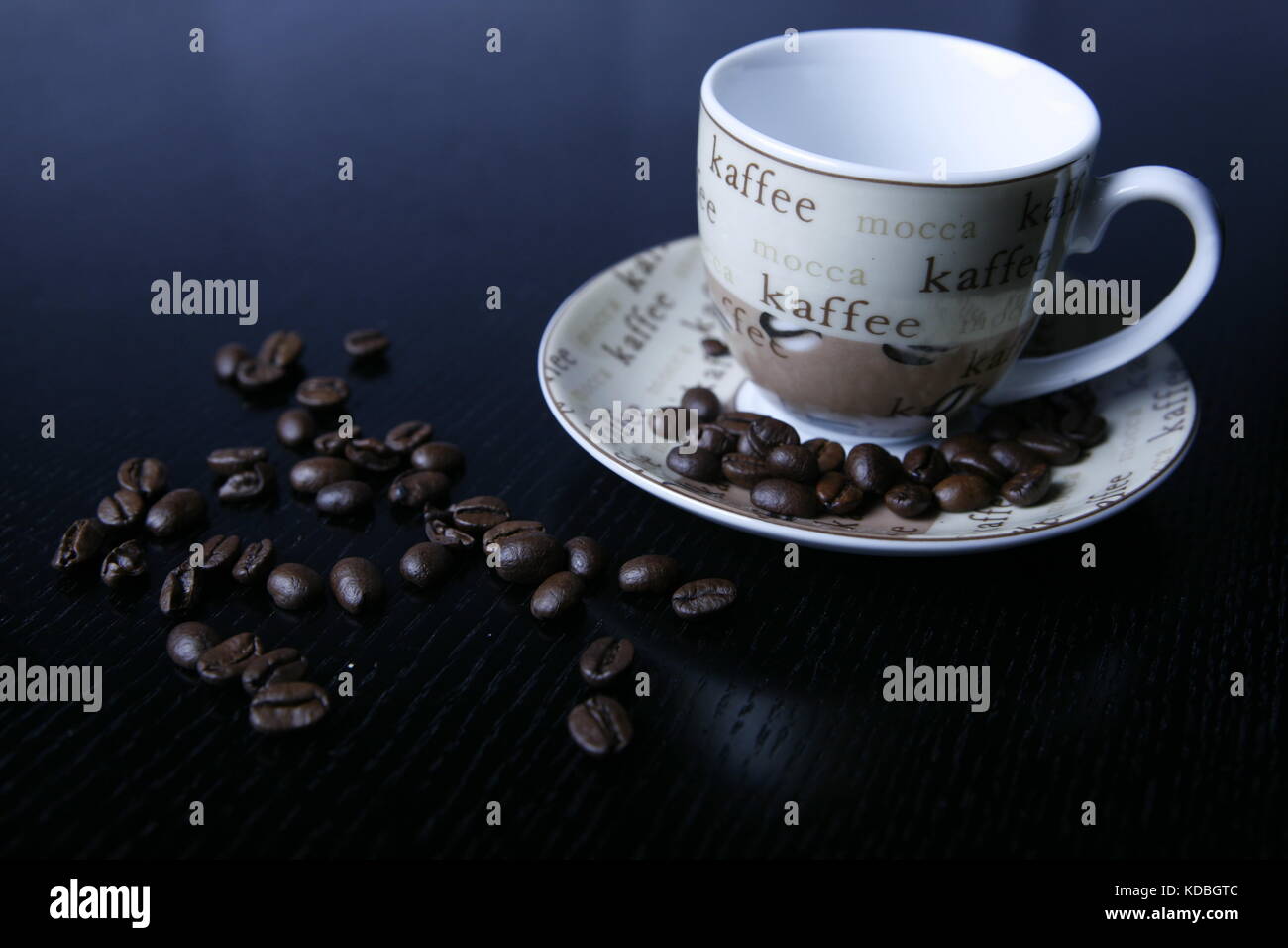 Moccatasse kaffeetasse verstreuten Kaffee Bohnen mit schwarzem auf tisch - Mocca taza taza de café con granos de café dispersos en black mesa Foto de stock