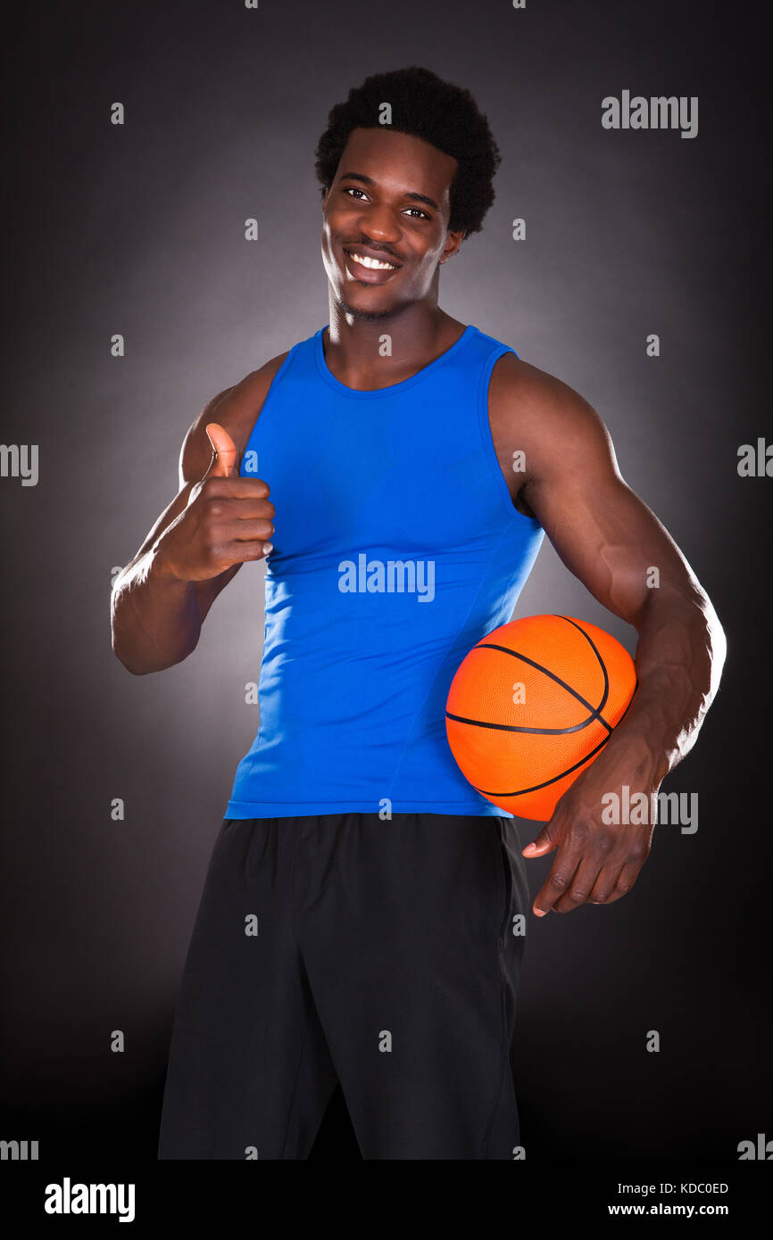 Hombre joven africano sosteniendo baloncesto sobre fondo negro Foto de stock