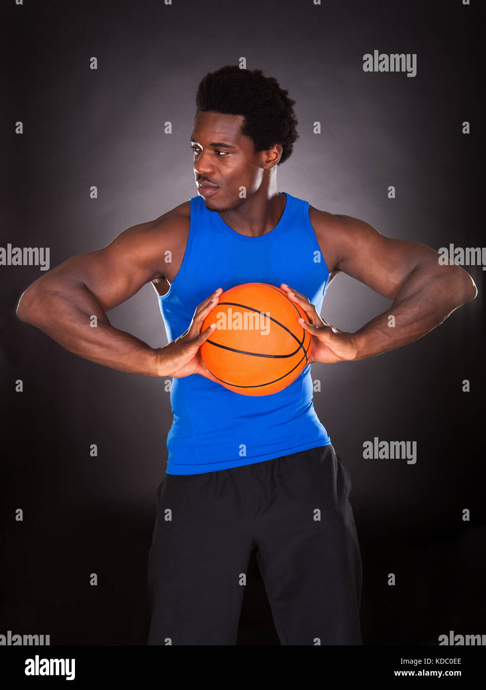 Hombre joven africano sosteniendo baloncesto sobre fondo negro Foto de stock