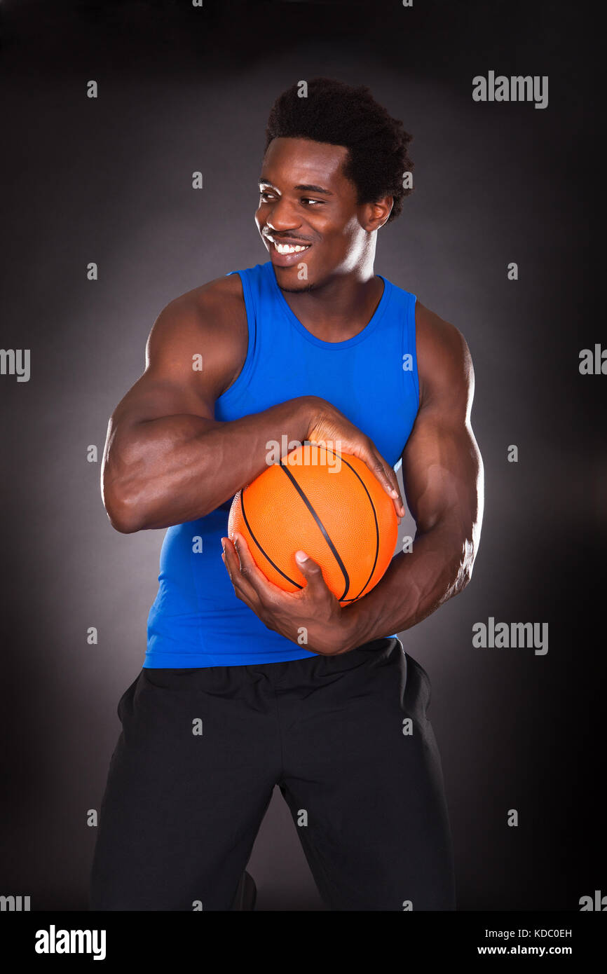 Hombre joven africano sosteniendo baloncesto sobre fondo negro Foto de stock