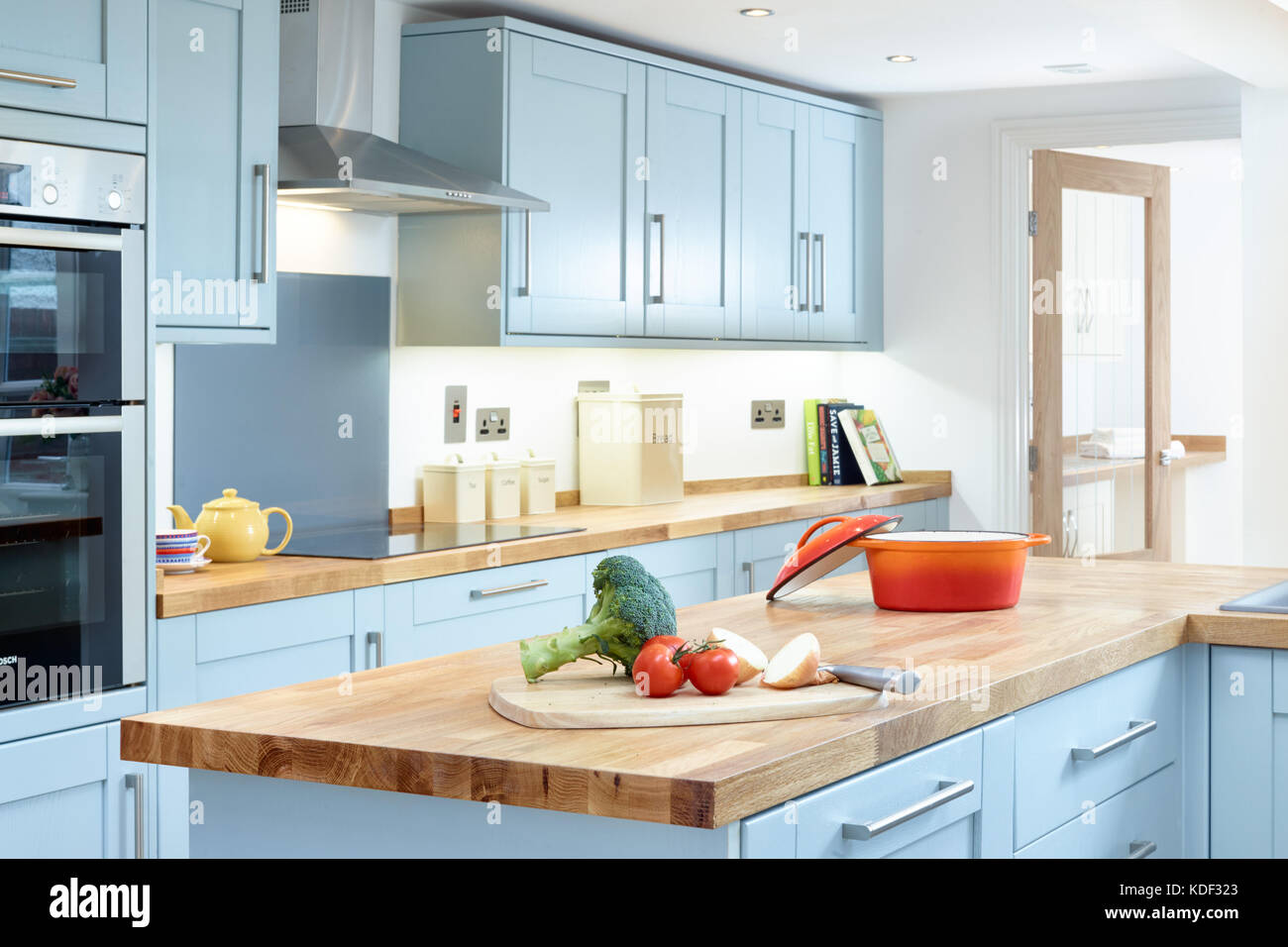 Un nuevo, moderno, de color azul, cocina de diseño de estilo shaker mostrando gabinetes, electrodomésticos y encimera con alguna preparación de comida. Foto de stock